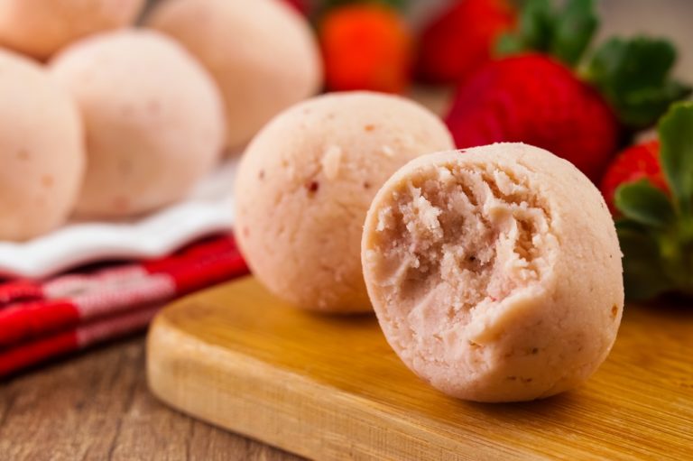 A picture of prepared strawberry fat bombs, one with a bite taken from it.